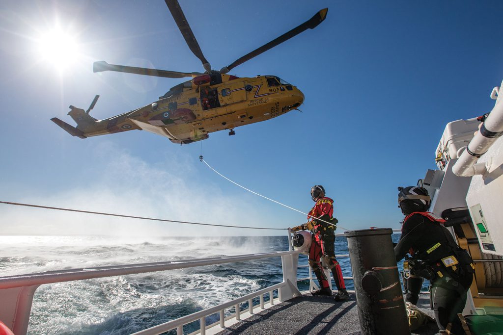A man watches a helicopter fly low above an icy ocean from his ship.