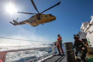A man watches a helicopter fly low above an icy ocean from his ship.