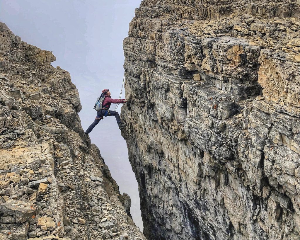 Climber makes wide step over crevasse