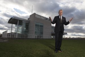 Alex Trebek stands on a lawn with the Royal Canadian Geographic Society headquarters in the background