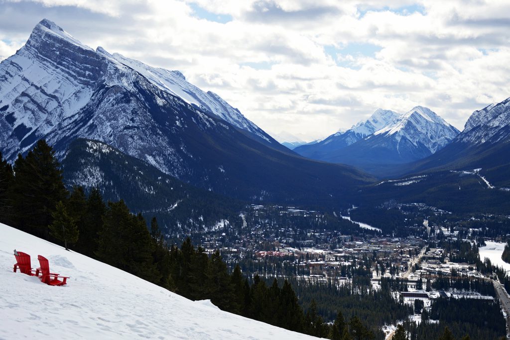 Parks Canada red Muskoka chairs on a snowy slope overlooking the Banff townsite