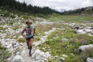 Filsan Abdiaman, a black woman, runs through a rockey valley of pink wildflowers.