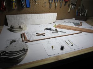 The work table with finished parts, plans, tools, and materials for the construction of a model of the iron storage tank located in Terror's stern.